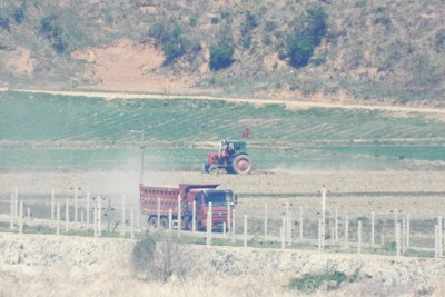 北朝鮮南西部・黄海北道の農村。トラックや農業用のトラクターが土ぼこりをあげて走っている＝韓国北西部・坡州市から2026年4月24日午前10時43分、福岡静哉撮影（超望遠カメラを使用）