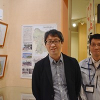 引田城を復元したイラスト2作品の展示コーナーのそばに立つ八木さん（左）と香川県東かがわ市教委の猪熊全徳さん＝同市歴史民俗資料館で2026年4月16日午後2時31分、佐々木雅彦撮影