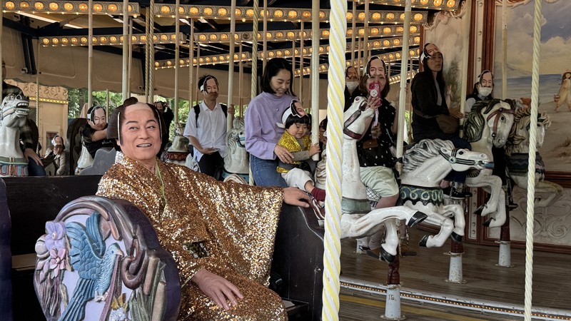 マツケンのお面をつけた観客と一緒にメリーゴーラウンドに乗るマツケンこと松平健さん＝横浜・八景島シーパラダイスで27日、國枝すみれ撮影