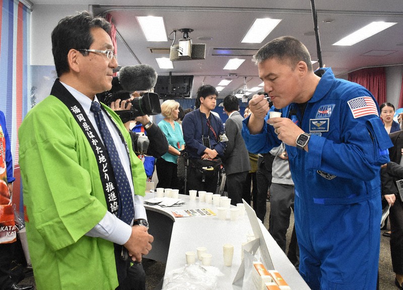 福栄組合の中垣誠社長（左）の前で、宇宙日本食に認証された「はかた地鶏ともち麦のお粥」を試食するチェル・リンドグレン宇宙飛行士＝福岡市中央区の福岡アメリカンセンターで2026年4月28日、宗岡敬介撮影