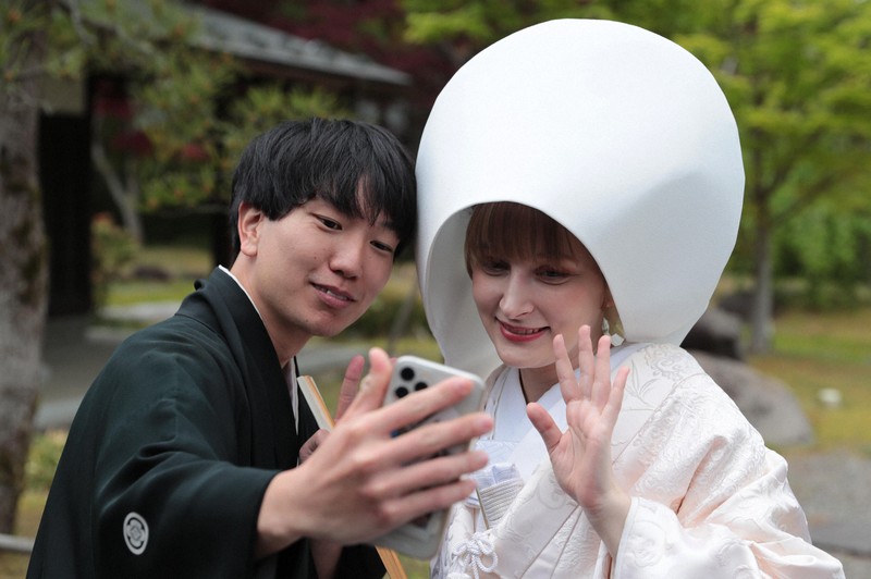 花嫁道中を終え、白むくに着替えたサヴェンコ・ヴァレリヤさん（右）は比留間希星さんと一緒にウクライナにいる父親のオレクサンドルさんとビデオ通話をして花嫁姿を見せた＝石川県七尾市で2026年4月29日午前10時59分、岩本一希撮影