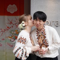 花嫁道中を終え、ウクライナの民族衣装に着替えたサヴェンコ・ヴァレリヤさん（左）と比留間希星さん。花嫁のれん（左奥）が架けられた2人の会社の事務所の前でサヴェンコさんは比留間さんのほおにキスをした＝石川県七尾市で2026年4月29日午前11時57分、岩本一希撮影