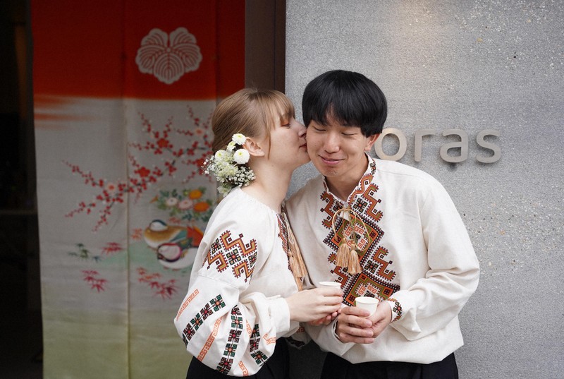 花嫁道中を終え、ウクライナの民族衣装に着替えたサヴェンコ・ヴァレリヤさん（左）と比留間希星さん。花嫁のれん（左奥）が架けられた2人の会社の事務所の前でサヴェンコさんは比留間さんのほおにキスをした＝石川県七尾市で2026年4月29日午前11時57分、岩本一希撮影