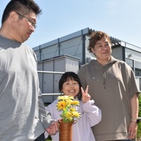 仮設住宅団地集会所で講演を終え、ヒマワリを手にポーズをとる菊地良さん（中央）を愛おしそうに見つめる 父修さんと母いつかさん＝石川県七尾市で、2026年5月2日午後2時31分、中尾卓英撮影