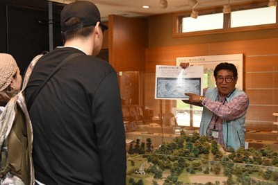 来館者に湯築城の魅力を説明する武田正俊さん（右）＝松山市の湯築城資料館で2026年4月17日午後1時58分、狩野樹理撮影