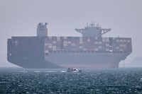 A container ship sits at anchor as a small motorboat passes in the foreground in the Strait of Hormuz off Bandar Abbas, Iran, May 2, 2026. (Amirhosein Khorgooi/ISNA via AP)