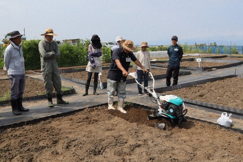 昨年のまいばら農業塾の様子。栽培アドバイザーの手本を見て、耕運機の使い方を学ぶ塾生たち＝米原市世継で2025年8月23日午前10時35分、長谷川隆広撮影