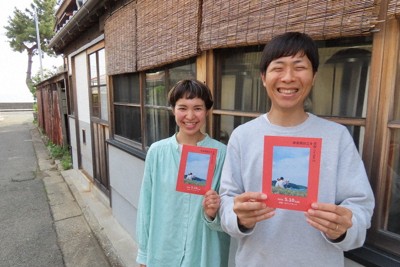 津屋崎海岸（左奥）そばのビール工房前でイベントチラシを見せる江藤彰洋さん（右）、瑶子さん夫妻＝福岡県福津市で2026年4月27日午後4時41分、荒木俊雄撮影