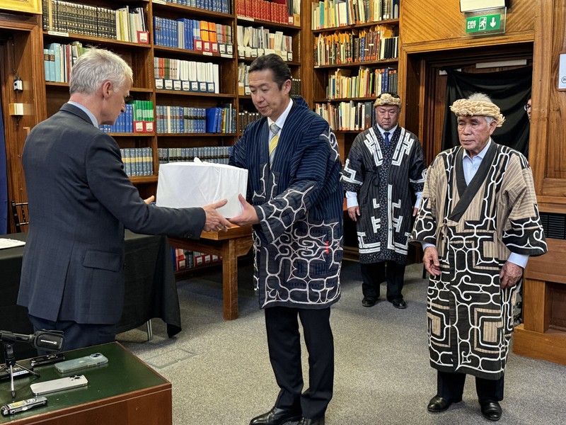 英自然史博物館のダグラス・ガー館長（左）からアイヌ民族の遺骨を受け取る黄川田仁志アイヌ施策担当相（中央）。右端は大川勝・北海道アイヌ協会理事長＝ロンドンで2026年5月5日、福永方人撮影
