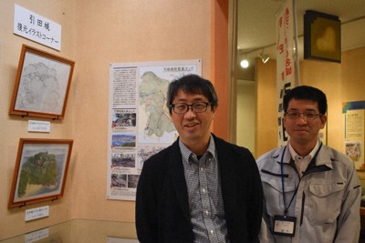 引田城を復元したイラスト2作品の展示コーナーのそばに立つ八木さん（左）と香川県東かがわ市教委の猪熊全徳さん＝同市歴史民俗資料館で2026年4月16日午後2時31分、佐々木雅彦撮影